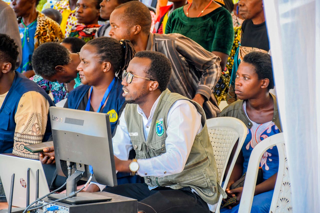 A diverse group of adults engaging with technology at a community event in Rwanda.